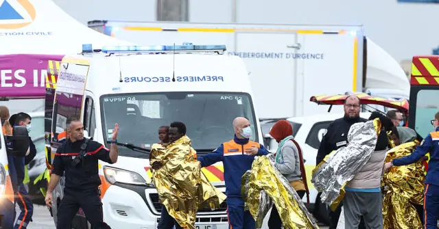 Emergency responders assist individuals wrapped in thermal blankets near an ambulance and other emergency vehicles.