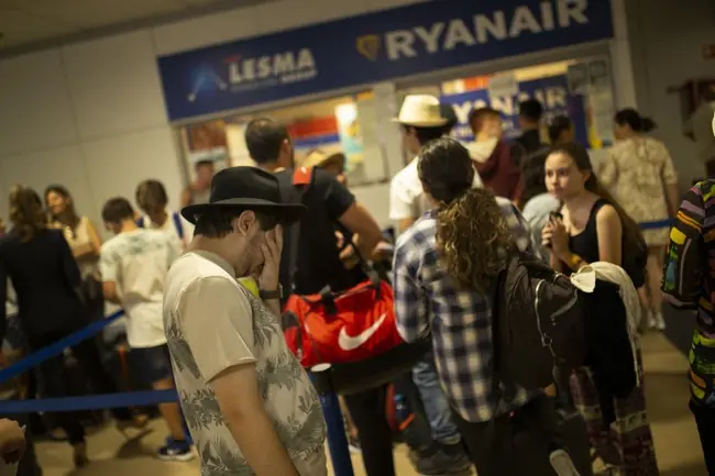 A group of people wait in line at an airport, with a Ryanair sign visible in the background.