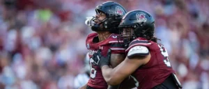 Two football players in maroon uniforms celebrate on the field during a game.