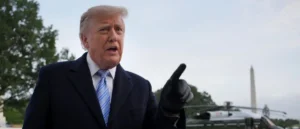 The image shows a person in a suit and tie, gesturing with their right hand, with the Washington Monument visible in the background.