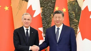 Two leaders in formal attire shake hands in front of flags, symbolizing diplomatic relations.