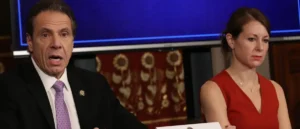 The image shows a man in a suit and a woman in a red dress, likely during a formal news or political event.
