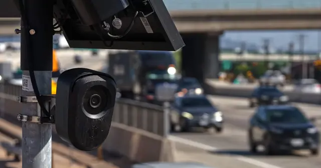 A traffic camera is mounted on a pole, monitoring a busy highway with multiple lanes of moving vehicles.