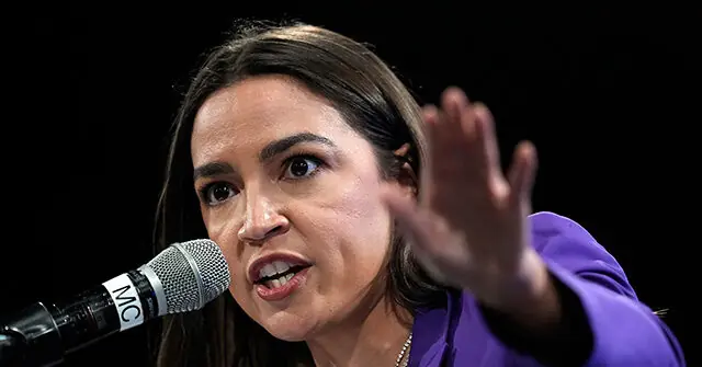 A woman in a purple outfit is speaking into a microphone, gesturing with her hand.