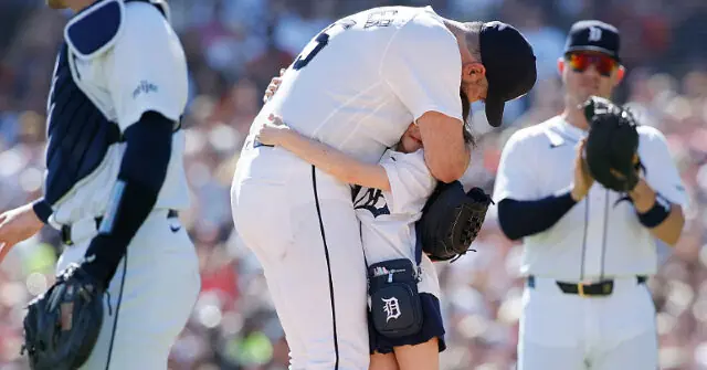 A baseball player is seen hugging a young fan during a game, with other players and a crowd in the background.