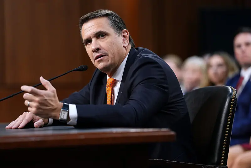 A man in a suit and tie is speaking at a formal event, gesturing with his hand as he addresses the audience.