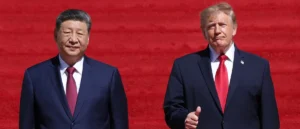 The photo shows two individuals in formal attire standing side by side against a red background.