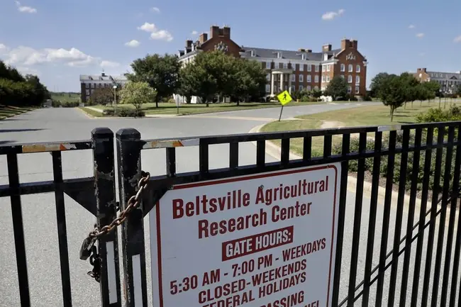 The image shows a locked gate with a sign for the Beltsville Agricultural Research Center, indicating gate hours and closed weekends and federal holidays.