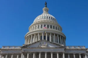 The image shows the United States Capitol building under a clear blue sky.