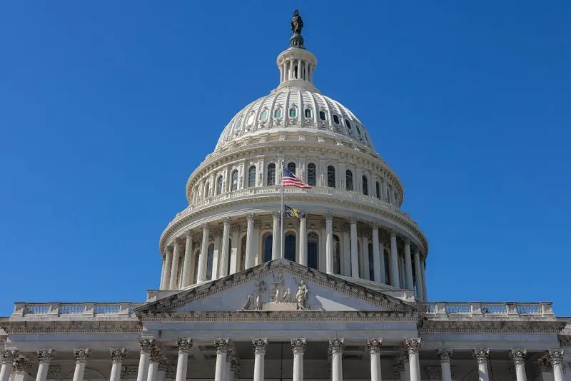 The image shows the United States Capitol building under a clear blue sky.