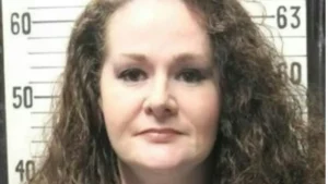 The image appears to be a mugshot of a person with curly hair, taken against a background with height measurement markings.