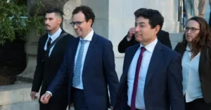 A group of formally dressed individuals, including men and a woman, are walking together in front of a building.