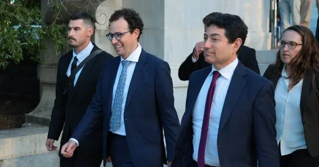 A group of formally dressed individuals, including men and a woman, are walking together in front of a building.