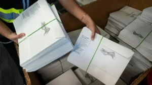 A person is handling stacks of official election mail envelopes, which are bundled with green string.