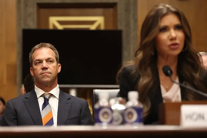 A man and a woman are seated at a table during a formal meeting or hearing, with the woman speaking into a microphone.
