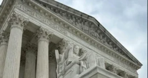 The image shows the exterior of the United States Supreme Court building, featuring intricate architectural details and a statue of a woman holding a book.