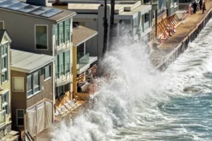 A powerful wave crashes against a coastal structure, threatening nearby buildings and infrastructure.