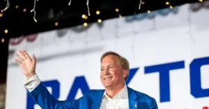 A man in a blue suit waves to the crowd at a campaign event.