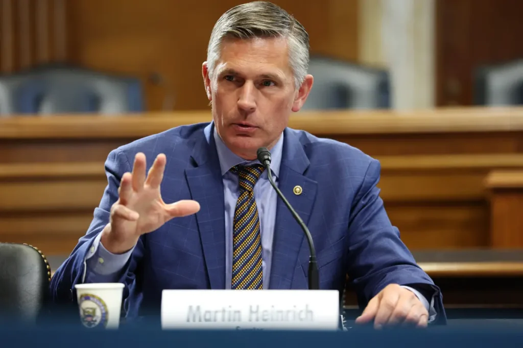 A man in a blue suit and tie is speaking at a formal event, gesturing with his hand.