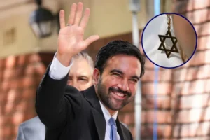 A man in a suit waves while wearing a Star of David necklace.