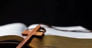 The image depicts a wooden cross resting on an open book, symbolizing faith and spirituality.