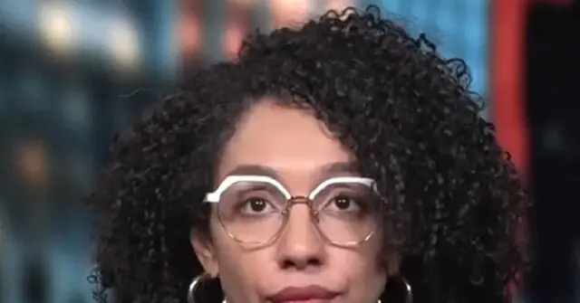 The image shows a person with curly hair wearing glasses and hoop earrings, set against a blurred background.