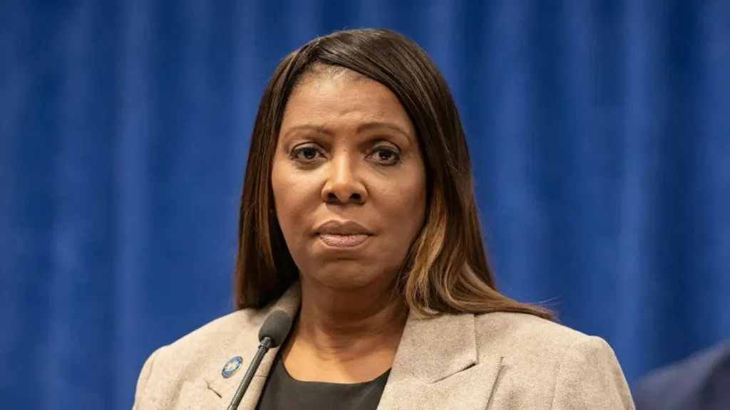 The image shows a person speaking at a press conference, with a microphone and a blue backdrop.