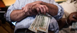 An elderly man holds a stack of $100 bills, symbolizing financial security or a significant financial transaction.