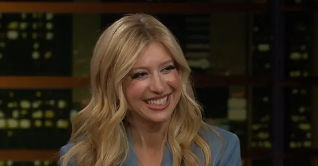 The image shows a person with long blonde hair smiling in a studio setting with control panels in the background.