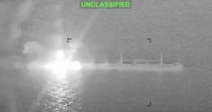 The image shows a nighttime military operation with a bright flash of light and smoke, likely from a missile or explosion, captured in thermal imaging.