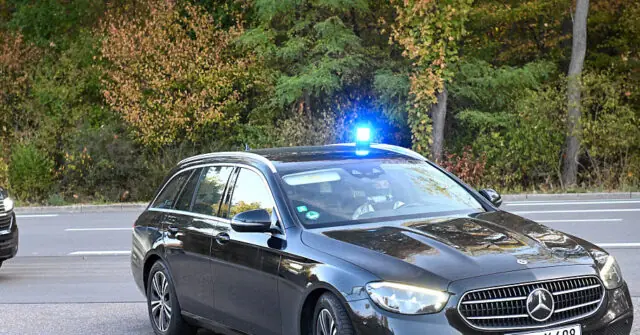 A police car with its lights activated is seen on a road, indicating an ongoing emergency or traffic situation.