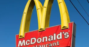 The image shows a McDonald's restaurant sign with the iconic golden arches and red background against a clear blue sky.