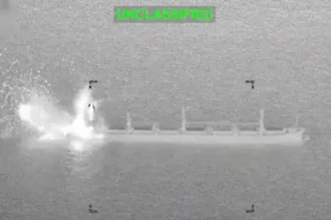 The image shows a military strike on a ship, with visible smoke and fire indicating an explosion or impact.