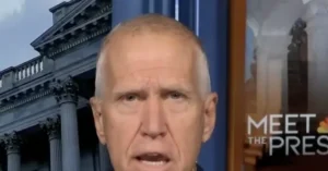 The image shows a man speaking on a news program, with a backdrop featuring a classical building and the text "MEET THE PRES."