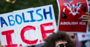 The photo shows a protest with signs advocating for the abolition of ICE (Immigration and Customs Enforcement).