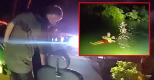 The image shows a nighttime rescue operation where a person is being pulled from the water by emergency responders.