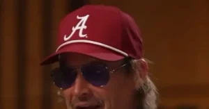 The image shows a person wearing a red cap with a white "A" and sunglasses, with a blurred background.