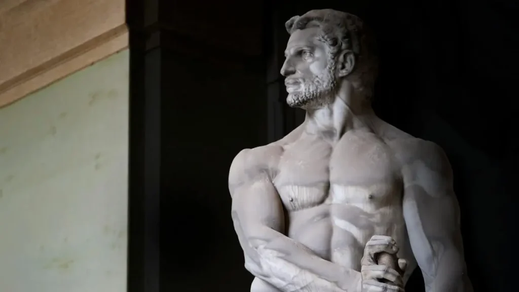 The image depicts a classical marble statue of a muscular male figure, likely representing a mythological or historical figure, standing with a confident posture.