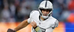 The image shows a football player in a white and black uniform, wearing a helmet, and holding a football, likely during a game.