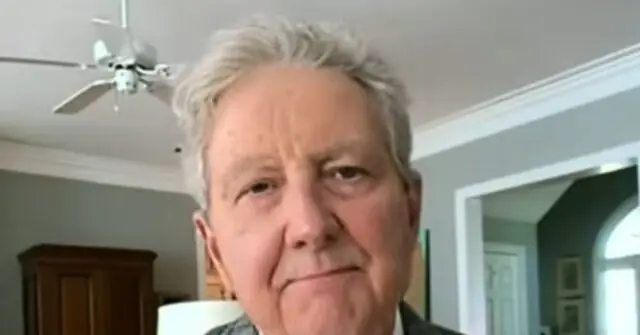 The image shows a person in a home setting, with a ceiling fan and a door visible in the background.