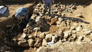 The photo depicts archaeologists working at an excavation site, carefully uncovering and examining ancient artifacts and structures.