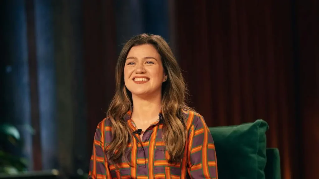 A woman in a colorful striped shirt is smiling while sitting on a green couch.