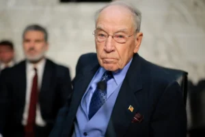 The image shows a man in formal attire, likely participating in a formal or official event, as indicated by the American flag pin on his lapel.