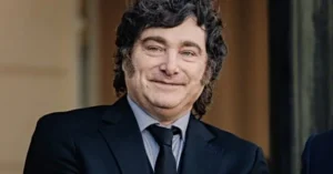 The image shows a man in a suit and tie, smiling, with a warm and friendly expression.