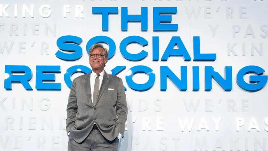 A man in a suit stands in front of a backdrop featuring the title "The Social Reckoning."