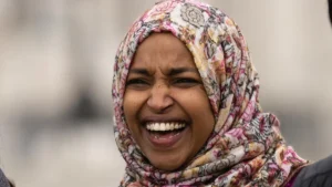 A woman wearing a floral hijab is laughing heartily in an outdoor setting.