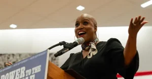 A woman is giving a passionate speech at a podium with a sign that reads "POWER TO THE PEOPLE."
