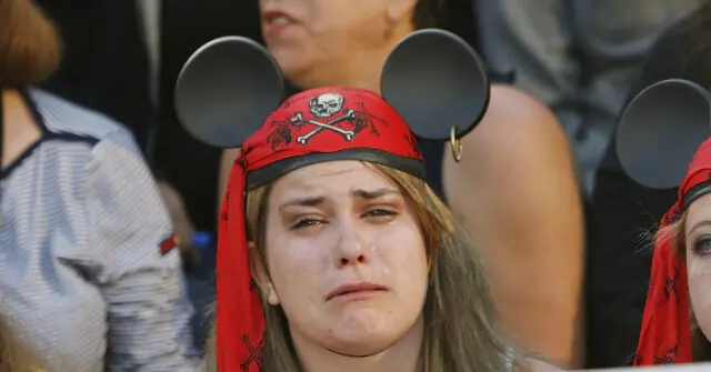 A person wearing a red pirate bandana and Mickey Mouse ears appears to be crying in a crowded setting.