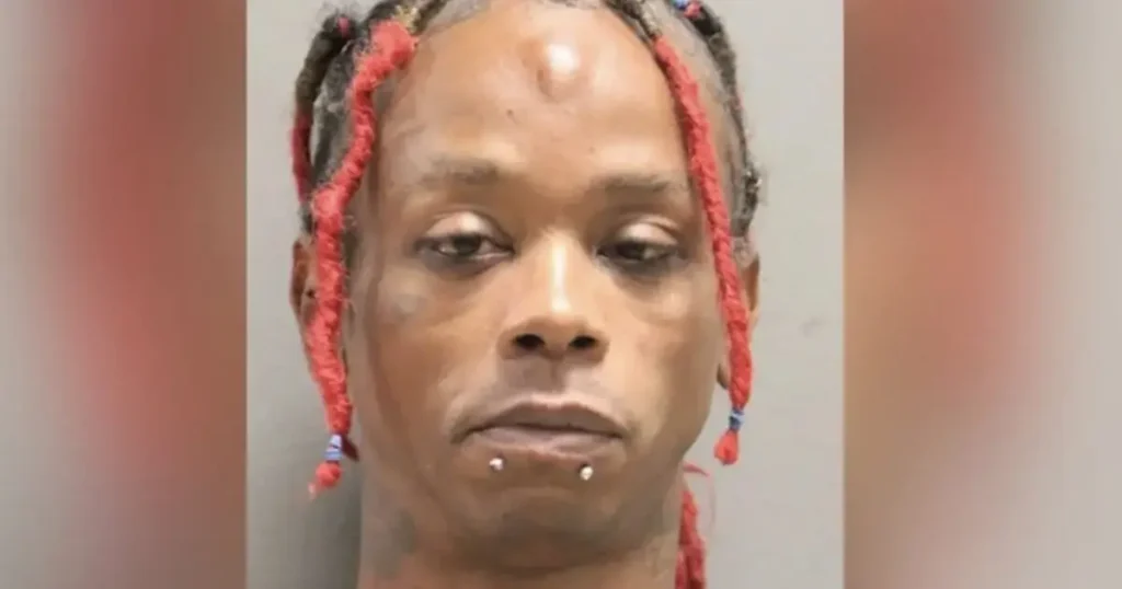 The image shows a person with red braids and facial piercings in a mugshot-style photograph.