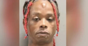 The image shows a person with red braids and facial piercings in a mugshot-style photograph.